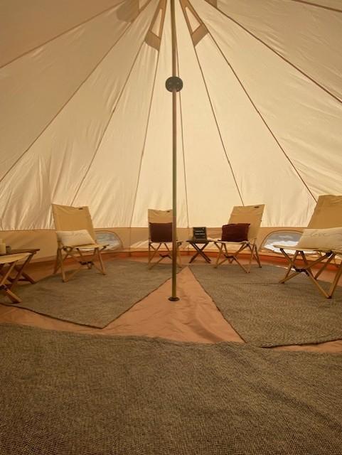 Interior of a large canvas tent with four chairs arranged in a circle around a central pole, small tables, and woven rugs on the floor.
